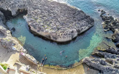 Tricase cosa vedere: una baia rocciosa con acque cristalline e persone che nuotano. Un luogo incantevole per godersi il mare.