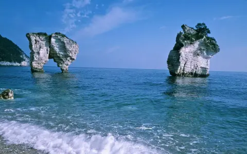 La **Baia delle Zagare** con le sue iconiche faraglioni bianchi che emergono dal mare blu intenso, sotto un cielo limpido.