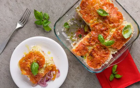 Una fetta di tiella pugliese di verdure, con riso, pomodori e cipolle rosse, guarnita con basilico fresco.