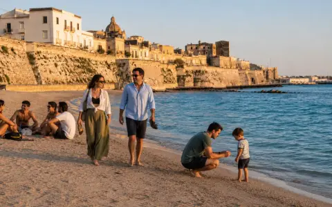 Famiglia passeggia sulla spiaggia di **Salento, Italia**, con un borgo storico sullo sfondo.