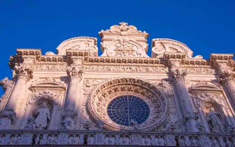 Facciata barocca di Lecce, con un grande rosone centrale e statue. Un esempio di cosa vedere a Lecce, tra arte e storia.