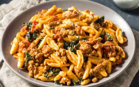 Un piatto di pasta con salsiccia sbriciolata, verdure e formaggio grattugiato, un sapore autentico dei primi piatti foggiani.