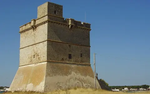 Torre costiera a Sant Isidoro, Salento. Antica sentinella di pietra contro il cielo azzurro, con il mare e il borgo sullo sfondo.