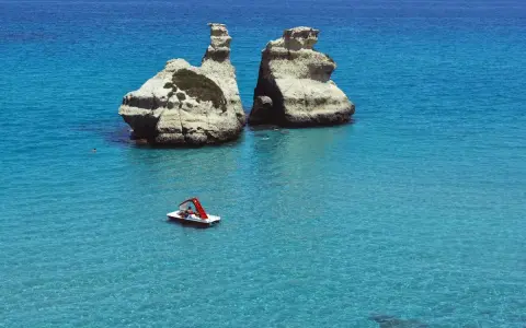 Due faraglioni bianchi emergono dal mare cristallino, con una pedalò che naviga vicino alla spiaggia dell'orso.