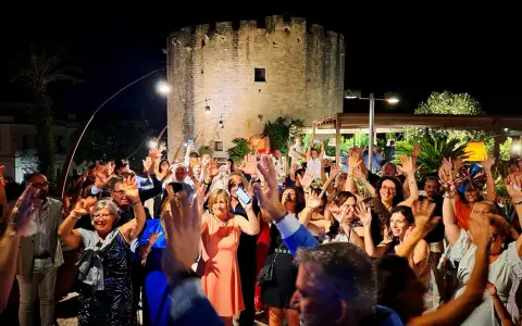 Festa con gente che alza le mani davanti a una torre antica, tipica delle sagre Salento agosto.