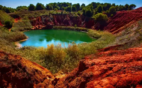 Un suggestivo lago di bauxite in Puglia, con acque verdi smeraldo circondate da rocce rosse e vegetazione lussureggiante.
