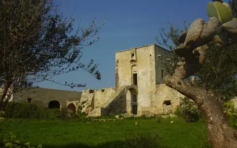 Antica masseria nella pianura salentina, con un torrione in pietra e vegetazione rigogliosa.