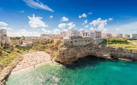Un borgo bianco su scogliere a picco sul mare turchese, una spiaggia affollata e un invito a scoprire la Puglia da visitare.