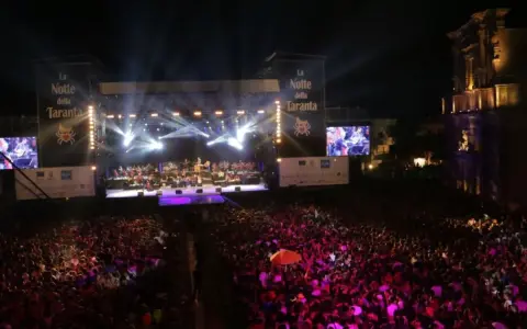 La Notte della Taranta, un'enorme folla festeggia sotto un palco illuminato. Le feste di settembre in Puglia sono magiche!