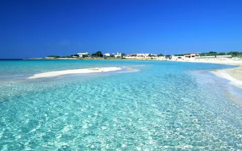 Acque cristalline lambiscono spiagge bianche, con un villaggio sullo sfondo sotto un cielo azzurro intenso.