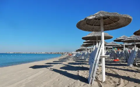 Ombrelloni di paglia e lettini bianchi sul lungomare Torre Lapillo, con il mare azzurro e il cielo limpido.