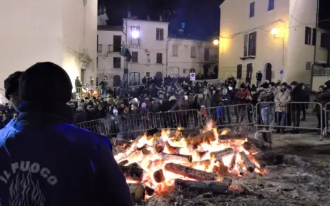 Grande falò nella piazza per la festa della birra Sant'Antonio Abate. La folla ammira le fiamme mentre un gruppo suona musica.