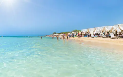 Spiaggia pugliese con acque cristalline e lettini sotto gazebo bianchi, ideale località mare Puglia per famiglie.