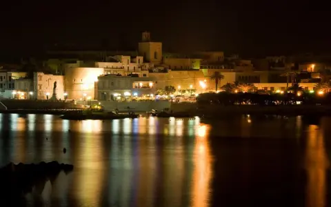 Otranto di notte: luci, castello e riflessi sull'acqua. La città si anima, pronta per le discoteche estive.