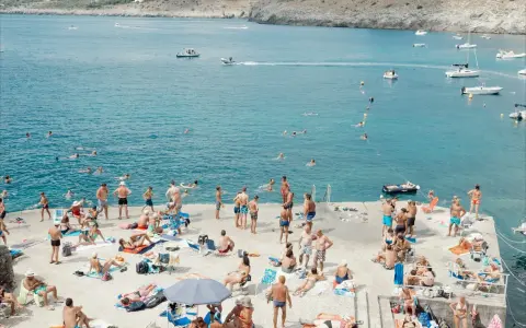 Gente in spiaggia e in mare a Santa Maria di Leuca, con barche all'orizzonte.