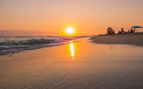 Tramonto dorato sulla spiaggia di Ugento, Salento. Famiglie rilassate sulla sabbia mentre il sole si specchia sul mare calmo.