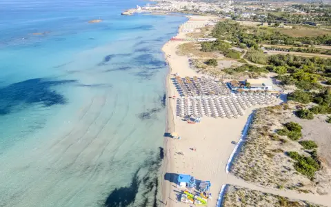 Spiaggia di Torre San Giovanni con ombrelloni e lettini, mare cristallino e vegetazione mediterranea.