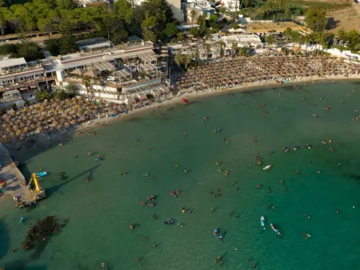 Vista aerea di una spiaggia affollata con ombrelloni e persone che nuotano nel mare cristallino, una delle spiagge più belle del mare di Taranto.