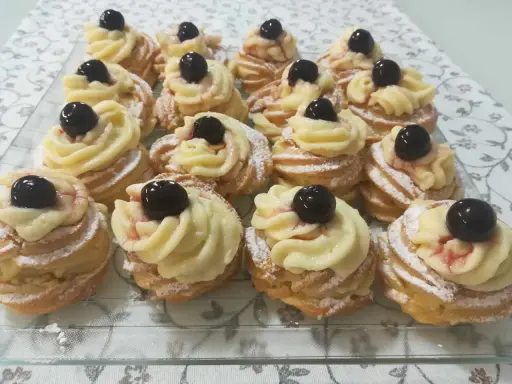 Zeppole pugliesi, dolci fritti con crema pasticcera e ciliegina, spolverati di zucchero a velo.