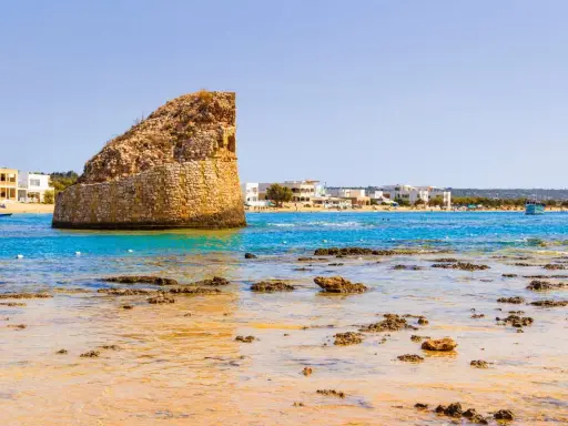 La torre pali di Lido Marini, con il mare cristallino e le case bianche sullo sfondo, evoca un'estate senza fine.