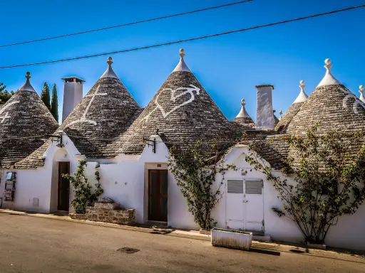 Trulli bianchi con tetti conici in pietra, un cuore disegnato su uno di essi, in un borgo tra i più belli d'Italia in Puglia.