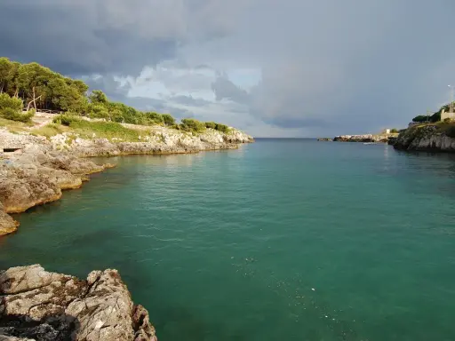 Baia rocciosa con acqua cristallina, alberi sulla costa. Un paesaggio che evoca i modi di dire salentini, come "fare la bella vita".