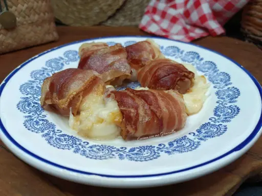Involtini di interiora pugliesi avvolti in pancetta croccante, serviti su un piatto bianco con decorazioni blu.