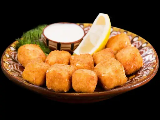 Croccanti cubetti di ricotta fritta salentina dorati, serviti su un piatto decorato con limone, salsa bianca e aneto.