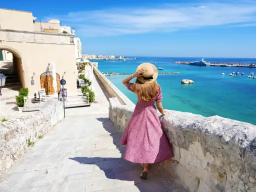 Una donna con cappello di paglia ammira il mare turchese e il porto di Otranto. Scopri cosa vedere in questo gioiello pugliese.