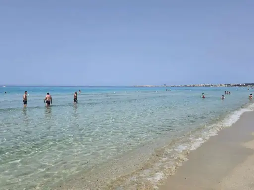 Persone in acqua cristallina vicino alla spiaggia di Gallipoli paese. Il mare calmo riflette il cielo azzurro.