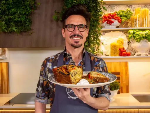 Chef sorridente con un piatto di torta salata, ispirata alle ricette leccesi, con pomodorini e basilico sullo sfondo.