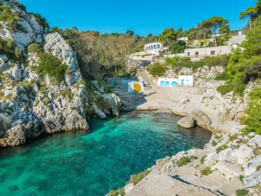 Baia incantevole con acque cristalline, perfetta per un tour Puglia 10 giorni. Case bianche e rocce a picco sul mare.
