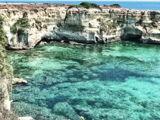 Scogliere bianche e acque cristalline, un paradiso tra le spiagge Puglia. Nuotatori si godono il mare turchese.