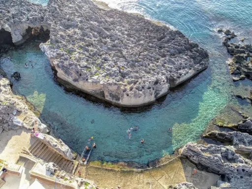 Tricase cosa vedere: una baia rocciosa con acque cristalline e persone che nuotano. Un luogo incantevole per godersi il mare.