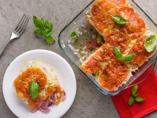 Una fetta di tiella pugliese di verdure, con riso, pomodori e cipolle rosse, guarnita con basilico fresco.