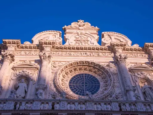 Facciata barocca di Lecce, con un grande rosone centrale e statue. Un esempio di cosa vedere a Lecce, tra arte e storia.