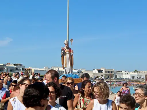 Festa San Foca: folla partecipa alla processione con la statua del santo su un carro, sotto un cielo azzurro.