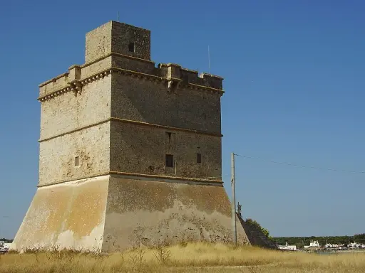 Torre costiera a Sant Isidoro, Salento. Antica sentinella di pietra contro il cielo azzurro, con il mare e il borgo sullo sfondo.