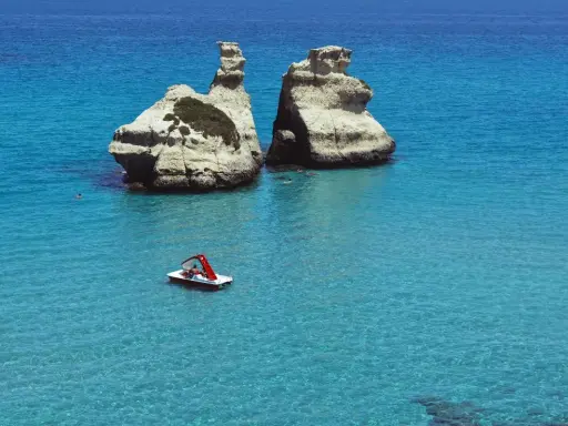 Due faraglioni bianchi emergono dal mare cristallino, con una pedalò che naviga vicino alla spiaggia dell'orso.