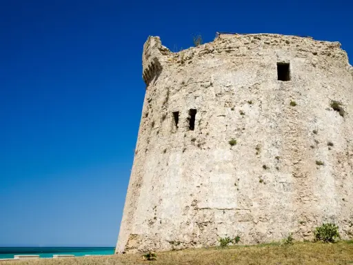 Antica torre mozza, con merli frastagliati, si erge contro un cielo blu intenso, testimone silenzioso di antiche storie.