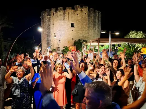 Festa con gente che alza le mani davanti a una torre antica, tipica delle sagre Salento agosto.