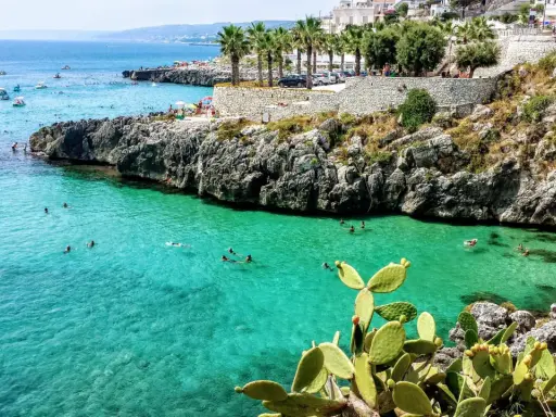 Splendida baia pugliese con acque cristalline e scogliere rocciose. Gente che nuota e si gode il sole, un vero paradiso per chi ama il **puglia mare**.