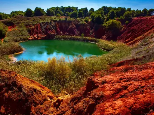 Un suggestivo lago di bauxite in Puglia, con acque verdi smeraldo circondate da rocce rosse e vegetazione lussureggiante.