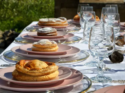 Tavola apparecchiata con bicchieri di cristallo e piatti rosa, su cui riposano dolci invitanti, tra cui una piscialetta leccese cosparsa di zucchero a velo.