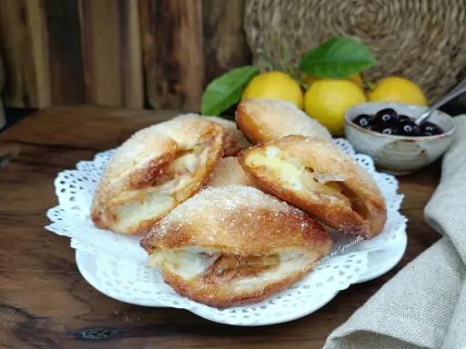 Monachine salentine dorate e zuccherate, un dolce profumato con ripieno di mele e un tocco di ciliegie.