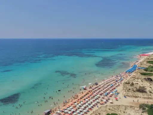 Spiaggia affollata con ombrelloni colorati e acque cristalline, le Maldive della Puglia dove si trovano per godersi il sole e il mare.