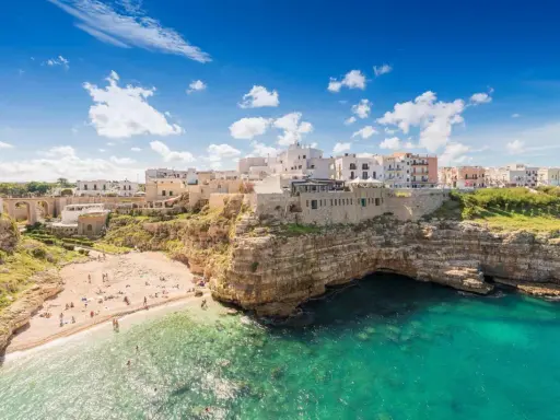 Un borgo bianco su scogliere a picco sul mare turchese, una spiaggia affollata e un invito a scoprire la Puglia da visitare.