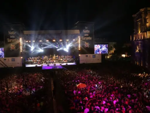 La Notte della Taranta, un'enorme folla festeggia sotto un palco illuminato. Le feste di settembre in Puglia sono magiche!