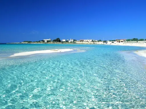 Acque cristalline lambiscono spiagge bianche, con un villaggio sullo sfondo sotto un cielo azzurro intenso.