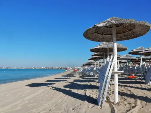 Ombrelloni di paglia e lettini bianchi sul lungomare Torre Lapillo, con il mare azzurro e il cielo limpido.